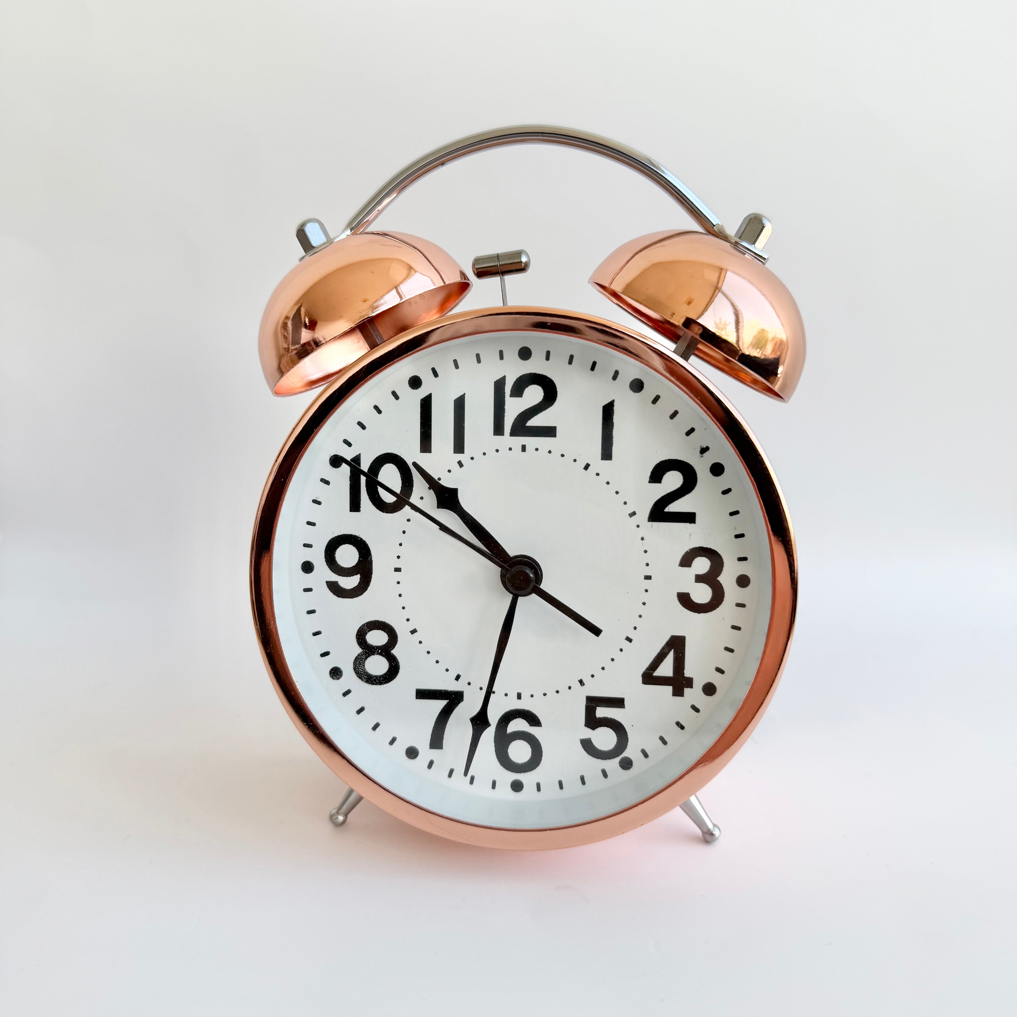 rose gold twin bell alarm clock with white face and black numbers on a clean background
