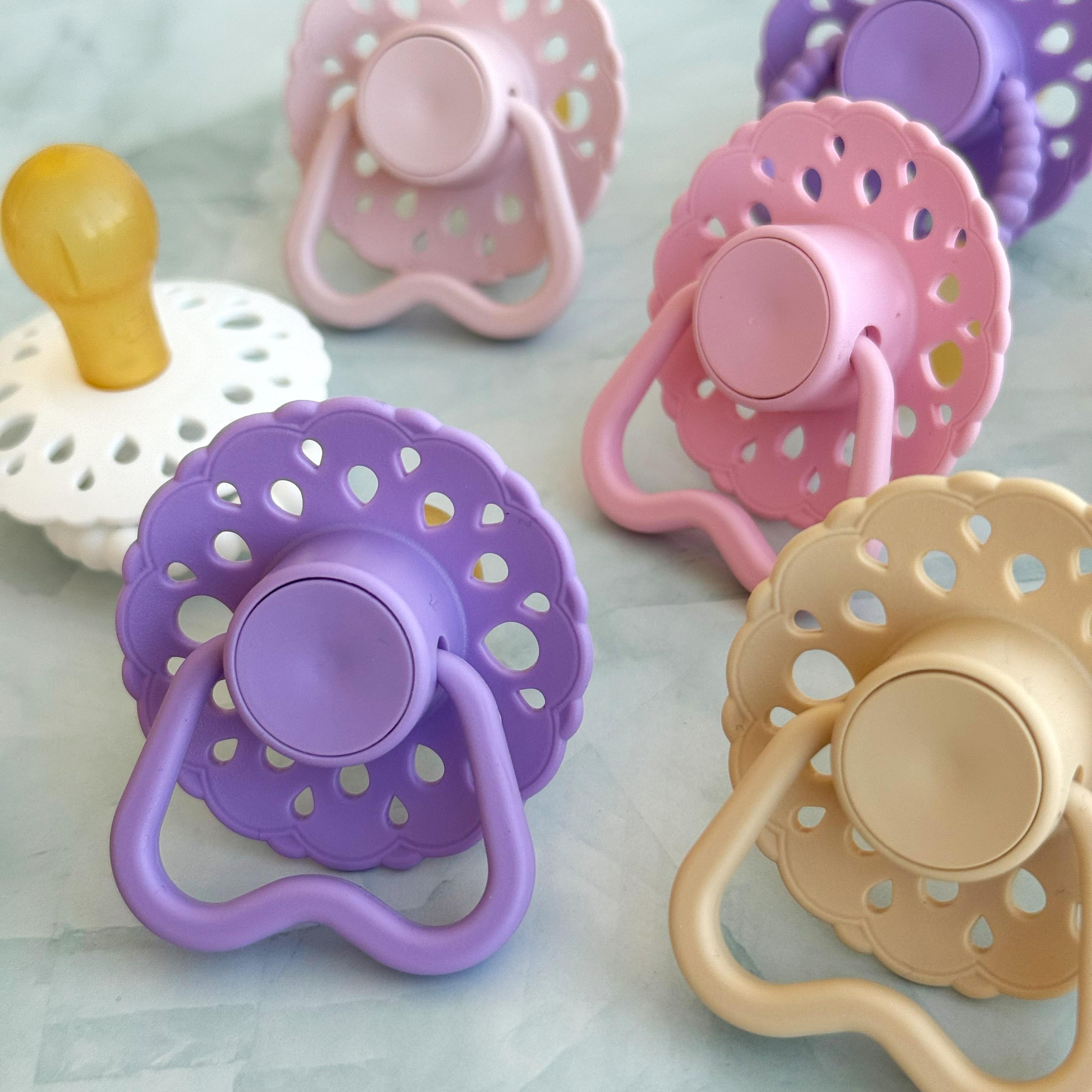Set of bloom baby dummies in pastel colours including oatmeal, blush, lavender, baby pink and white with hold me handles displayed on a wooden table