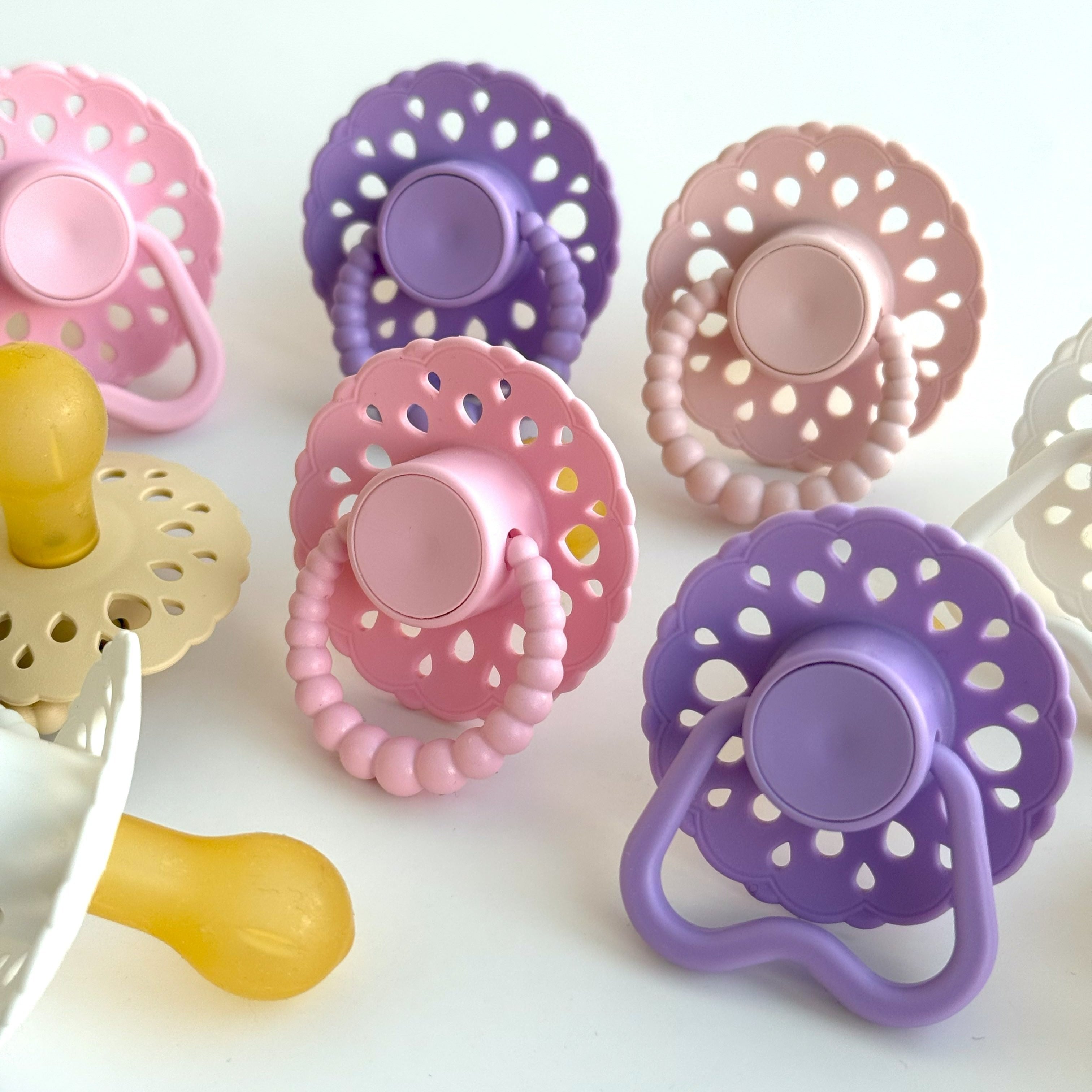 Set of bloom baby dummies in pastel colours including oatmeal, blush, lavender, pink and white displayed on a wooden table