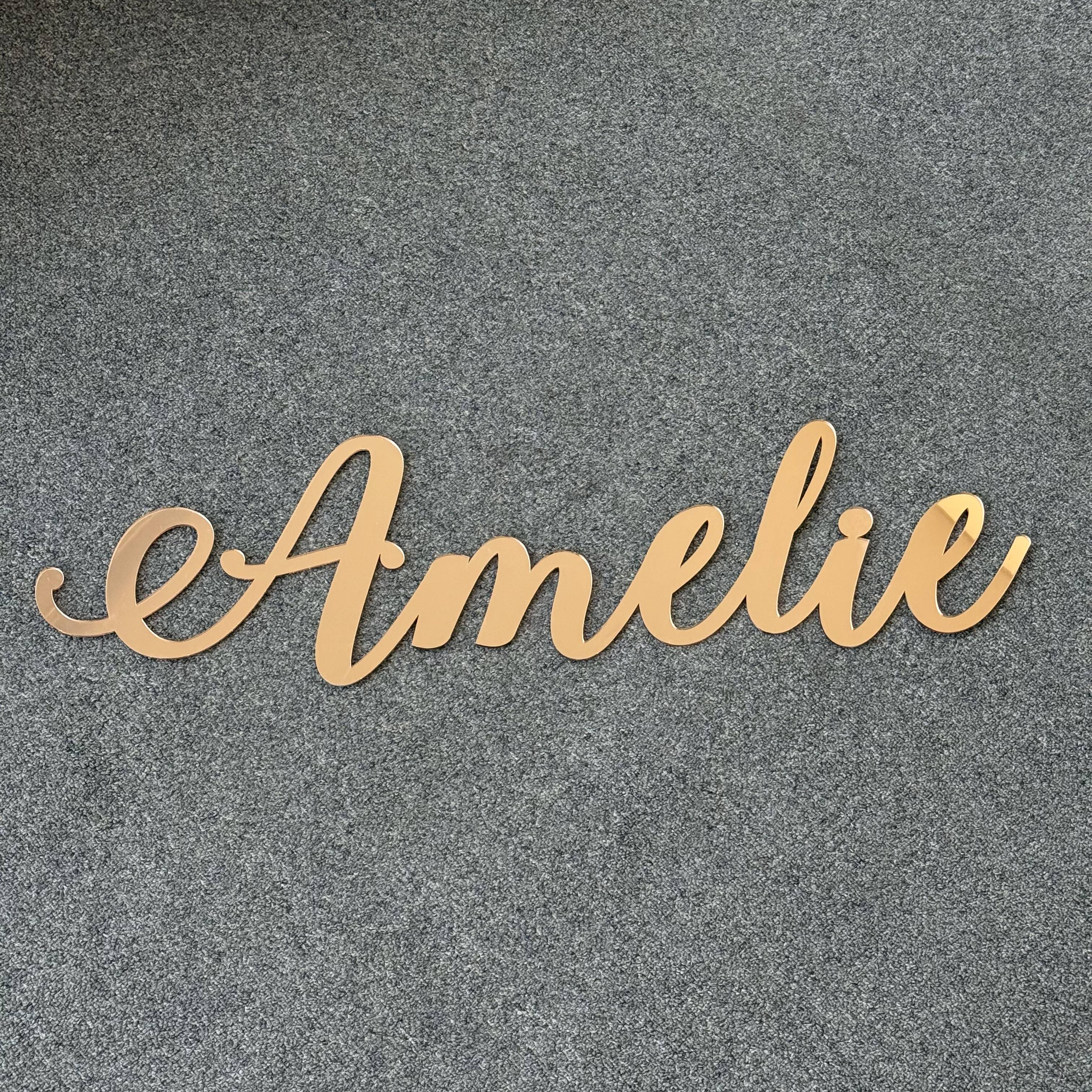 Personalised acrylic script name sign reading Amelie in gold, designed as elegant wall decor for a nursery or kids room