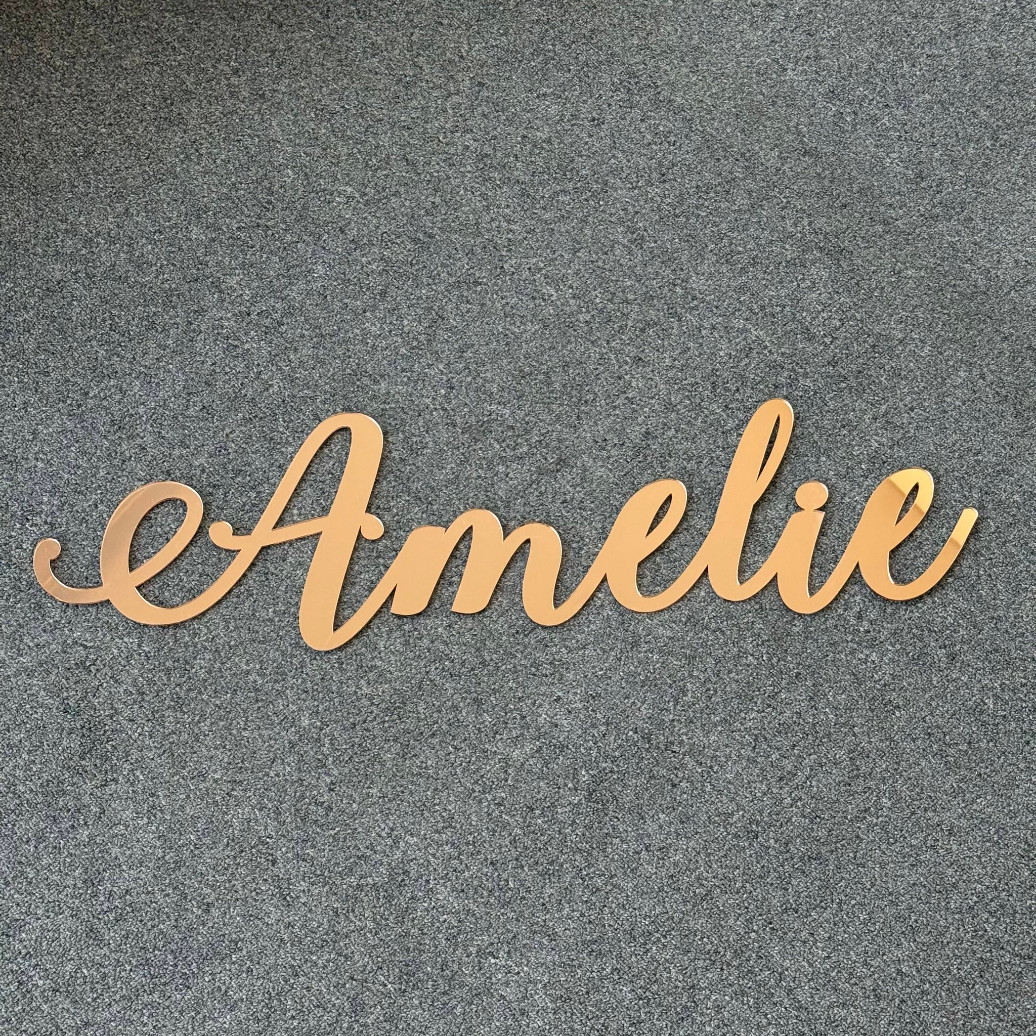 Personalised acrylic script name sign reading Amelie in gold, designed as elegant wall decor for a nursery or kids room