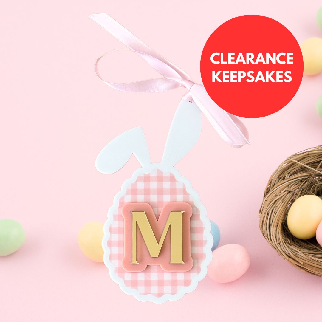 Personalised egg-shaped keepsake ornament with initial letter M, pink gingham design and ribbon, displayed with pastel Easter eggs and clearance keepsakes label
