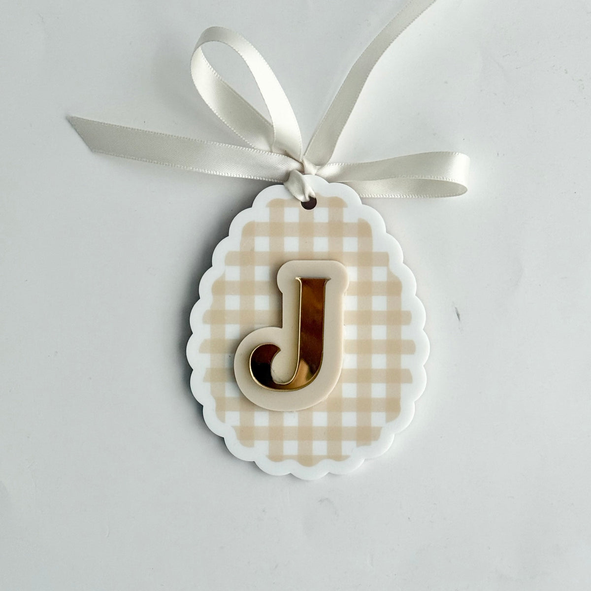 Personalised initial keepsake ornament with letter J in gold acrylic on beige gingham background, scalloped edge and ribbon hanger