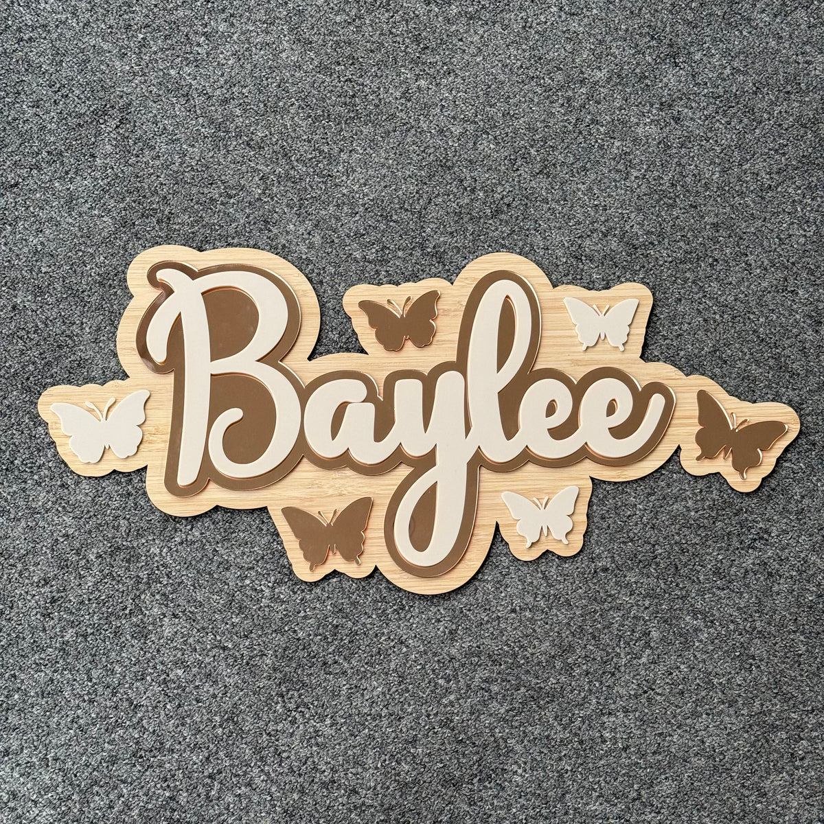 Personalised bamboo name plaque reading Baylee with layered script lettering and butterfly details, wooden nursery decor sign on grey background