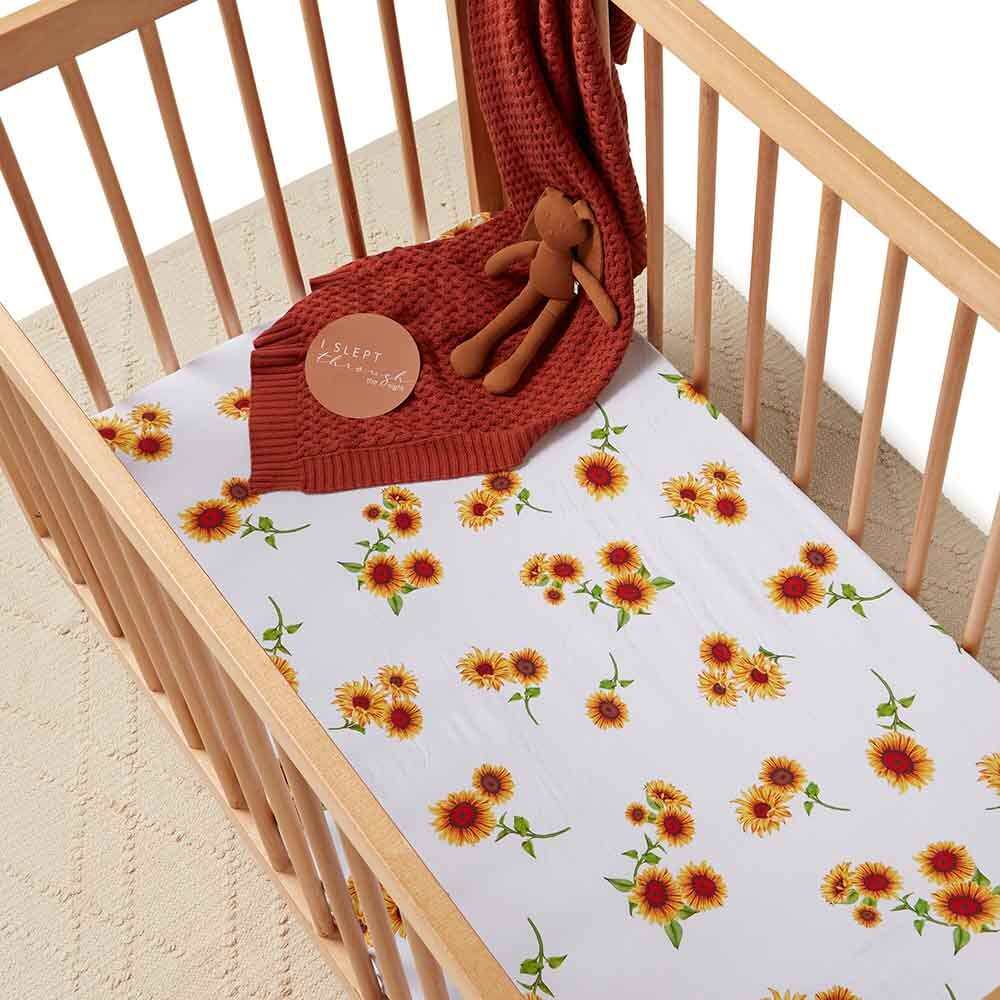 Baby cot with sunflower print fitted sheet and rust knitted blanket in a wooden nursery crib