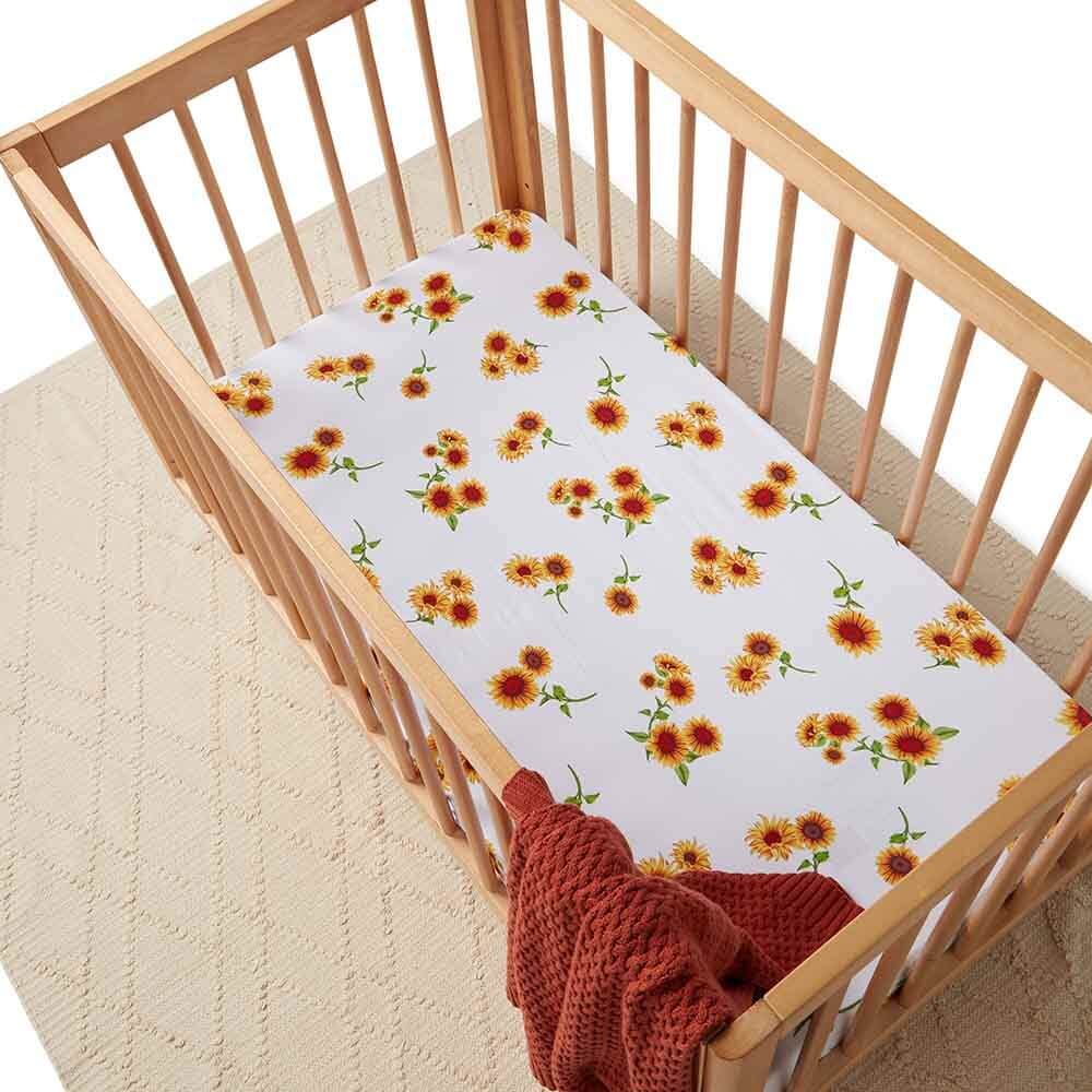Baby cot with sunflower print fitted sheet and rust knitted blanket in a wooden nursery crib