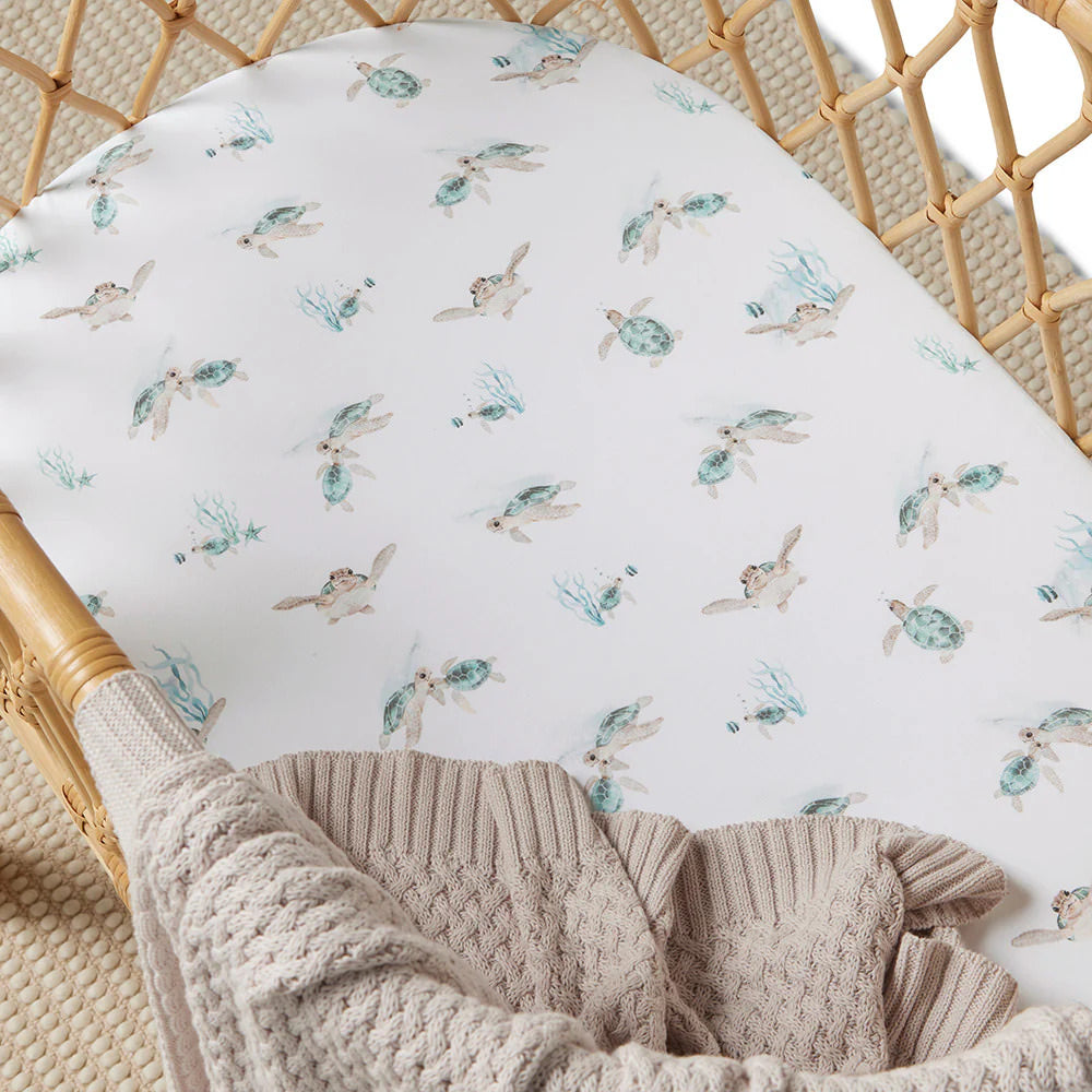 Baby bassinet with sea turtle print fitted sheet styled with knitted blanket.