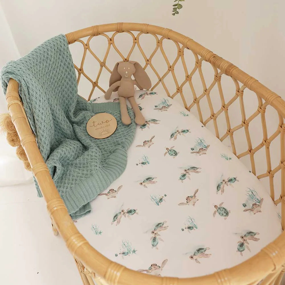 Baby bassinet with sea turtle print fitted bassinet sheet/ change pad styled with knitted blanket and soft toy in neutral nursery and bunny toy.