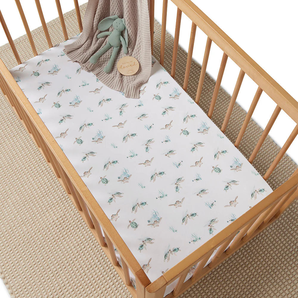 Baby cot with turtle print fitted cot sheet styled in a wooden crib with neutral nursery decor