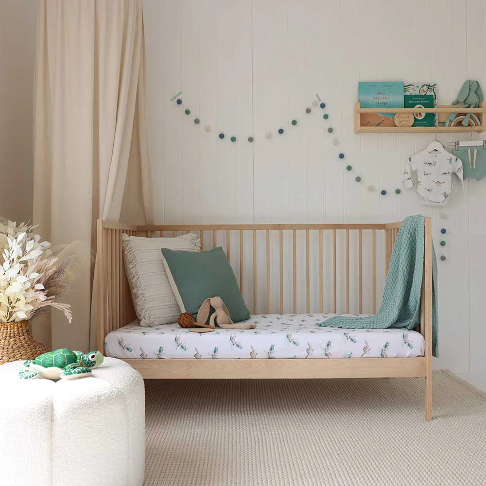 Baby nursery with wooden cot styled with turtle print cot sheet, teal blanket and ocean themed decor