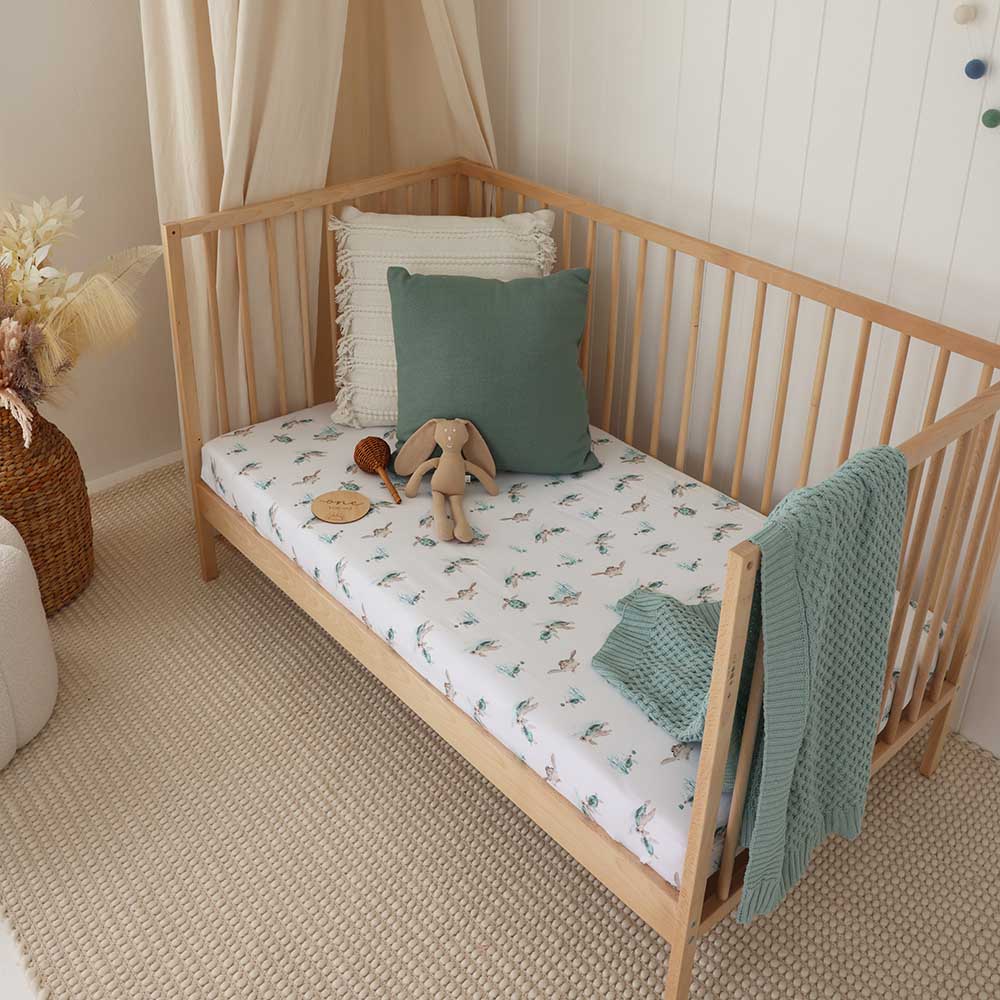Baby nursery with wooden cot styled with turtle print cot sheet, teal blanket and ocean themed decor