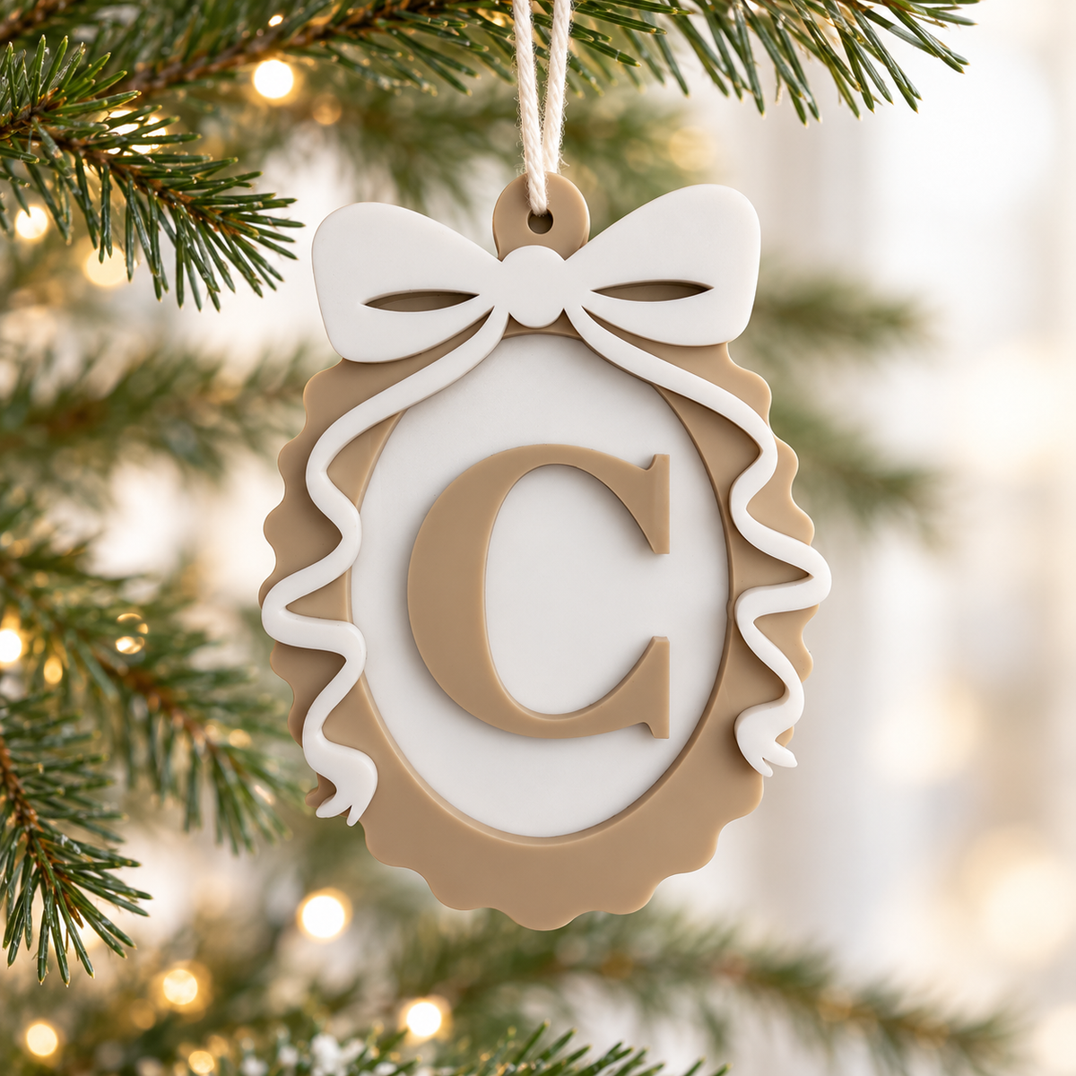 Personalised initial Christmas ornament with beige acrylic letter C, white bow and scalloped oval frame hanging on a Christmas tree